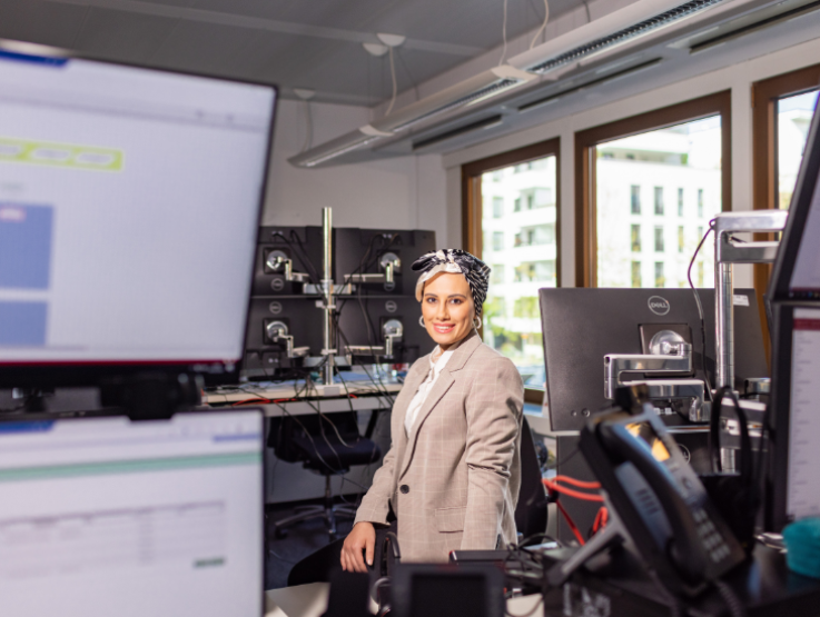 Frau steht in einem Büro, um sie herum sind Tische mit unzähligen Monitoren