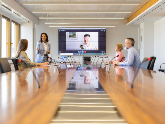 Transformation und Kultur Großer Sitzungssaal, in dem vier Mitarbeitende an einem langen Tisch sitzen und mit einem per Videokonferenz zugeschalteten Mitarbeitenden im Gespräch sind